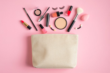 Wall Mural - Cosmetic bag and makeup products spilling out on pink background. Flat lay, top view