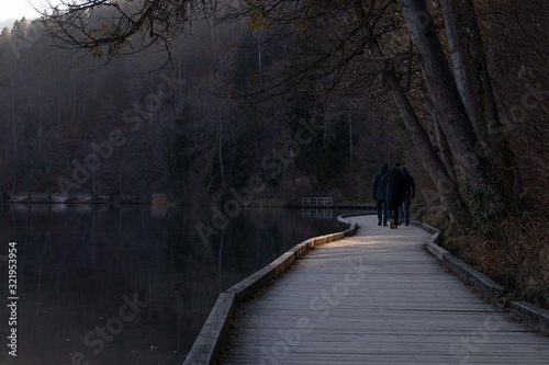 Cuadros en Lienzo Three men walking on the wooden boardwalk near the lake surrounded by bare trees
