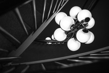 Greyscale Shot Of Illuminated Lamps Hanging Near Railings Inside A Building