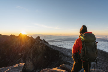 Wall Mural - a man with backpack enjoying sunrise over the clouds on kota kinabalu summit in malaysia. travel lif