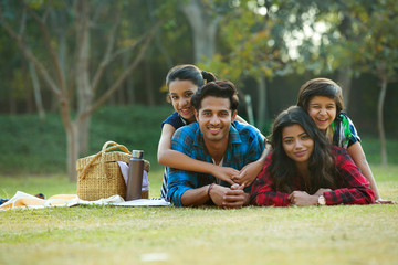 Happy man and woman on a picnic lying down in garden beside a picnic basket and their children lying on their backs.