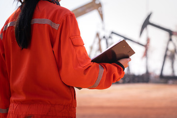 Woman supervisor or safety officer is holding the checklist document, prepare to perform safety audit and inspection. Photo taken with background of beam pump (oil pump) in well-site.