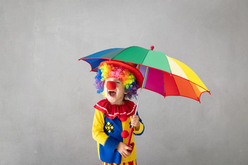 Funny kid clown playing against grey background