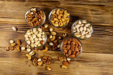 Sticker - Assortment of nuts on wooden table. Almond, hazelnut, pistachio, walnut and cashew in glass bowls. Top view. Healthy eating concept