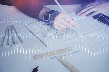 Double exposure of man's hands writing notes of stock market with forex chart.