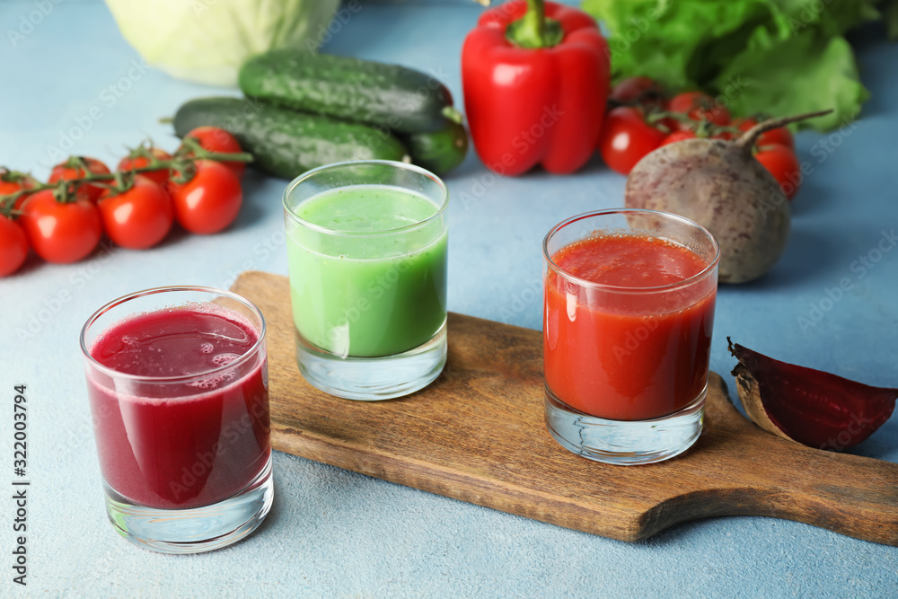 Glasses of fresh vegetable juices on color background