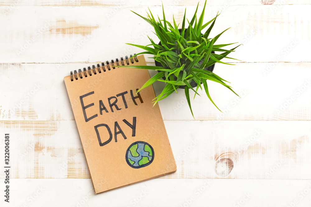 Notebook with text EARTH DAY and plant on light wooden background