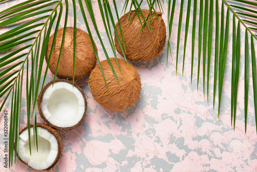 Ripe coconuts and palm leaves on color background