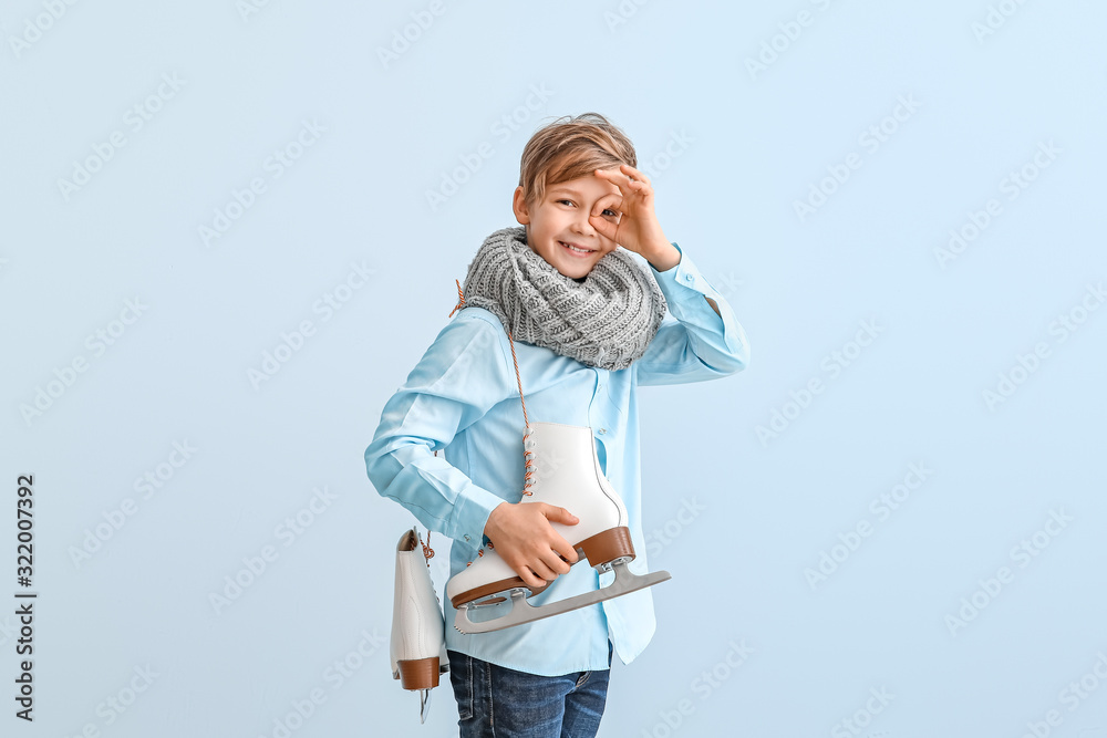 Cute little boy with ice skates against color background