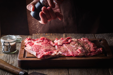 Wall Mural - Man cooking meat steaks on kitchen. Chef salt and pepper meat on wooden background