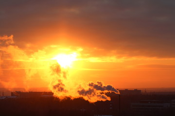 Wall Mural - red sun at sunset or dawn at dusk low above the horizon shrouded in smoke from the chimneys of the p