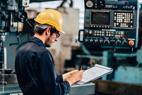 Fotomural young profession technician engineer operate heavy machine to automated CNC in factory, worker with check list