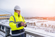 © Serhii - A smiling caucasian builder in a white hard hat and yellow fluorescent jacket holds clipboard