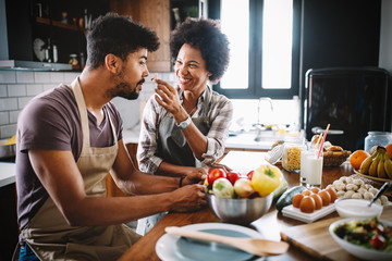 Wall Mural - Beautiful young couple having fun and laughing while cooking in kitchen