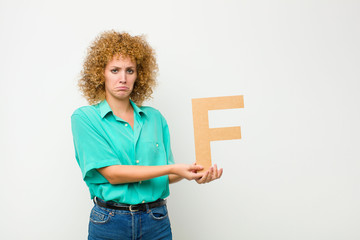 young pretty afro woman sad, depressed, unhappy, holding the letter F of the alphabet to form a word or a sentence.