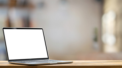 Fototapete - Computer laptop with white blank screen putting on the modern working table with blurred comfortable office as background. Void screen for advertise concept.