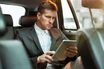 Wall Mural - young businessman reading world daily news while sitting in his car on his way to office, multitasking concept