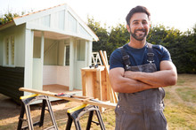Portrait Of Male Carpenter Building Outdoor Summerhouse In Garden