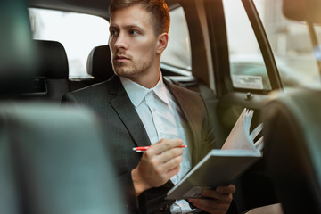 Wall Mural - young successful businessman takes notes to his planner while sitting in his car on the way to meetting with partners, multitasking concept