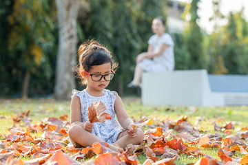 Canvas Print - Portrait Of A Girl Sitting In Colorful Fall Leaves at park with her mother.