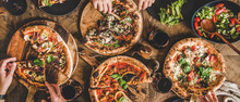Family Or Friends Having Pizza Party Dinner. Flat-lay Of People Eating Various Kinds Of Italian Pizza And Drinking Wine Over Wooden Table, Top View, Wide Composition. Fast Food Lunch Concept
