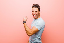Young Arabian Man Feeling Happy, Satisfied And Powerful, Flexing Fit And Muscular Biceps, Looking Strong After The Gym Against Pink Wall