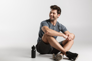 Smiling young sportsman sitting isolated over gray