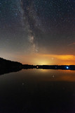 Fototapeta Niebo - A night on the lake with a bright milky way in the sky and millions of stars glittering in the water