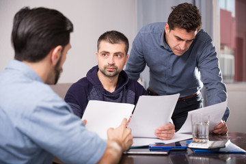 Three upset males with papers at table