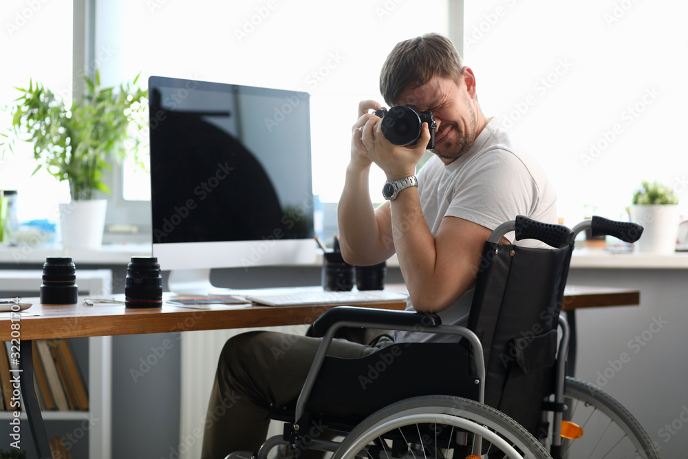 Male disabled photographer holds camera in his hands and takes picture portrait. Striving for a goal and self-sufficiency concept. Strong life position - obrazy, fototapety, plakaty 