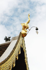 Golden naga and bells hanging on Art Roof of Buddhist temple with blue sky in Thailand