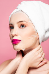 young woman in moisturizing face mask touching neck isolated on pink