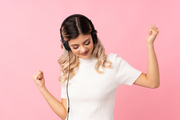 Wall Mural - Teenager girl over isolated pink background using the mobile with headphones and dancing