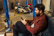 © Тарас Нагирняк - serious man using smartphone while male technician repairing his car in the garage