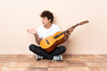 Wall Mural - Young caucasian man with a guitar sitting on the floor with surprise facial expression