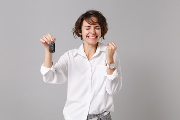 Smiling young business woman in white shirt posing isolated on grey wall background studio portrait. Achievement career wealth business concept. Mock up copy space. Doing winner gesture hold car keys.