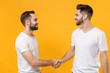 © ViDi Studio - Smiling young men guys friends in white blank empty t-shirts posing isolated on yellow orange background studio portrait. People lifestyle concept. Mock up copy space. Meeting, greeting with hands.