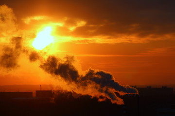 Wall Mural - red sun at sunset or dawn at dusk low above the horizon shrouded in smoke from the chimneys of the p