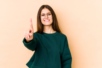 Young caucasian woman isolated on beige background showing number one with finger.