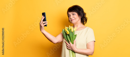 Photographie Beautiful old woman with professional smokey make-up and hairstyle holding tulip flowers on the pink background