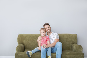 Wall Mural - Happy young father and daughter sitting on sofa near light wall