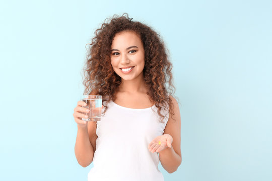 Young woman with fish oil and glass of water on color background