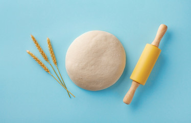 Wall Mural - Dough with rolling pin and wheat ears on blue background top view. Bakery concept. Flat lay.