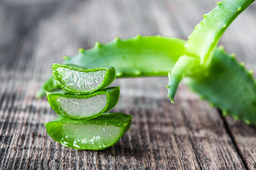 Fresh aloe vera leaves and slices of aloe vera on a wooden background.