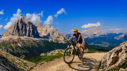 Tourist cycling in Cortina d'Ampezzo, stunning rocky mountains on the background. Woman riding MTB enduro flow trail. South Tyrol province of Italy, Dolomites.