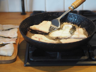 Home cooking. Fry river fish with pike slices in a black pan on a gas stove. Prepare the filling for the pie.