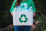 Fototapeta  - A woman collecting garbage and holding a recycle bin with plastic bottles in the outdoors