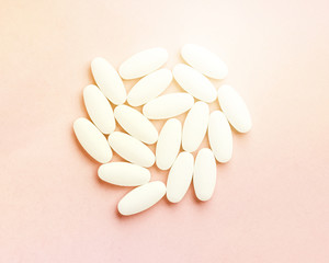 Circle shaped medical white oval pills close-up isolated on pink background.