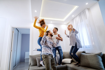 Group of cheerful best friends having fun at home. They are jumping on sofa and laughing.