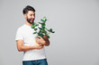 Handsome smiling young man holding potted plant isolated on grey background